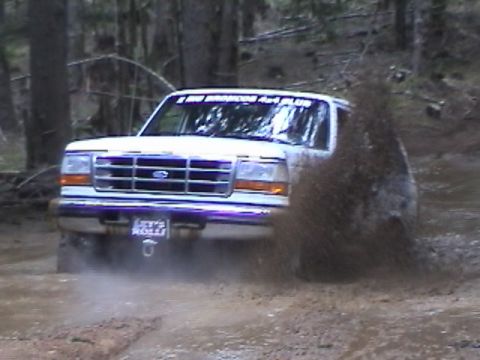 1994 Ford Explorer - A white Ford Bronco navigates a muddy trail, sending a spray of dirt into the air.