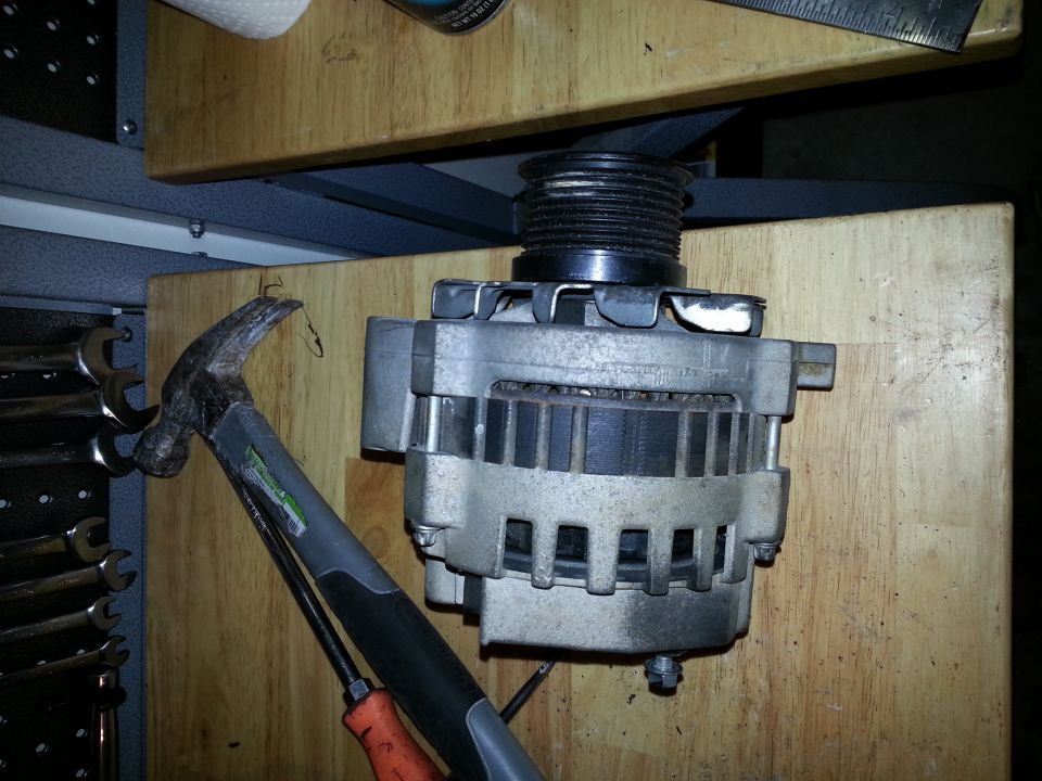 Alternator with hammer and screwdriver on wooden surface. SuperMotors logo visible