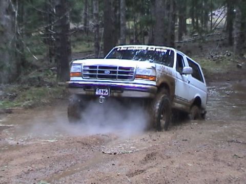 1994 Ford Explorer - A white SUV navigates a muddy trail in a wooded area, kicking up dust and dirt.