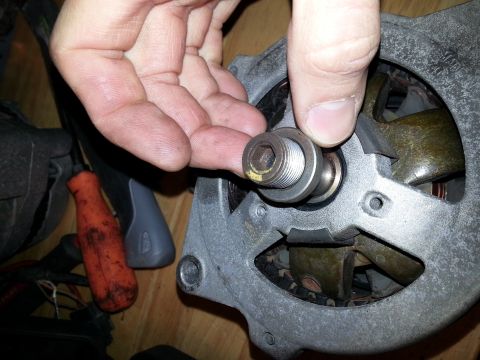 1994 Ford Bronco - A hand holds a component of an alternator, showing a hex bolt head and threaded shaft.