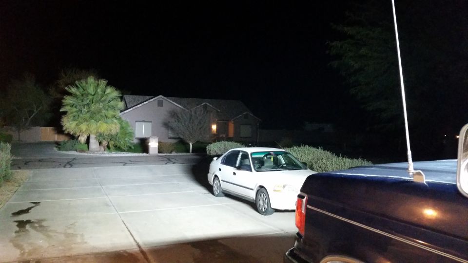 Dark blue Ford Bronco parked at night, white sedan in front, antenna visible.