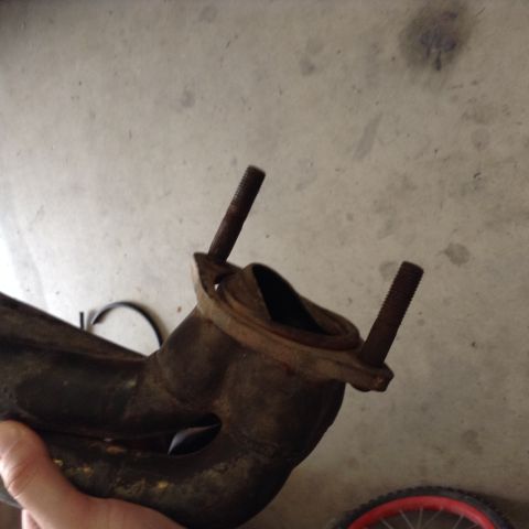 1991 Ford Bronco - A close-up shot shows a rusty exhaust manifold with two threaded studs protruding from a flange. The manifold is dark brown and appears to…