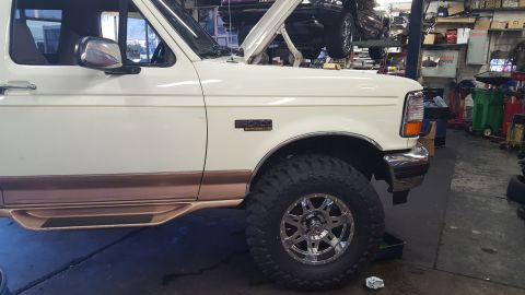 1995 Ford Bronco - The side view of a white Ford Bronco shows its chrome side mirror, a "BRONCO" emblem on the fender, and a large off-road tire with a chrome…