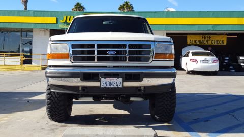 1995 Ford Bronco - Front view of a white Ford Bronco parked in front of a business with a green and yellow facade. The vehicle has a California license plate…