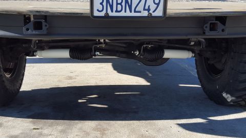 1995 Ford Bronco - The underside of a vehicle's rear suspension is shown, featuring white shock absorbers and black bellows. A license plate with the text "3N…