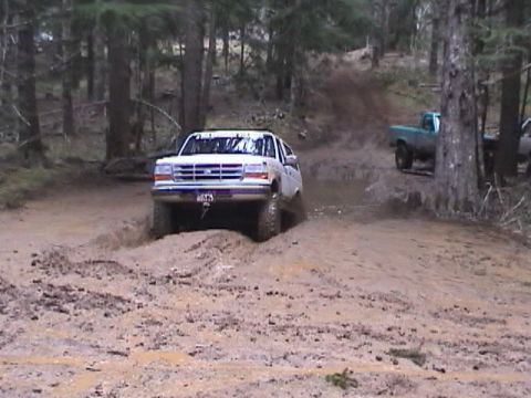 1994 Ford Explorer - A white Ford Bronco navigates a muddy trail with another truck visible in the background.