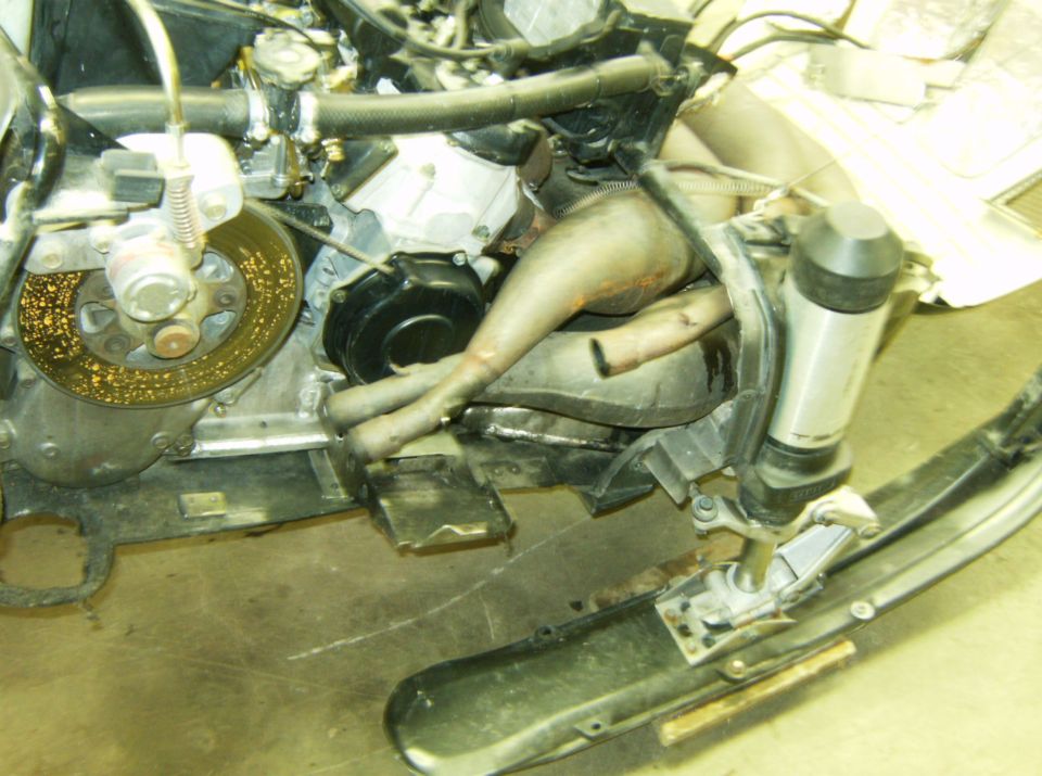 Snowmobile engine compartment with exhaust pipes, brake disc, and suspension.