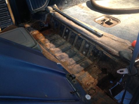1979 Ford Bronco - The interior of a vintage vehicle shows significant rust damage on the floor pan, particularly in the passenger footwell area. A metal bar…