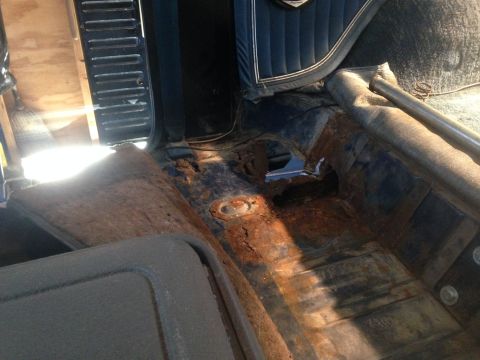 1979 Ford Bronco - The interior of a classic vehicle shows significant rust damage on the floorboards, with large holes exposing the undercarriage. A metal ba…