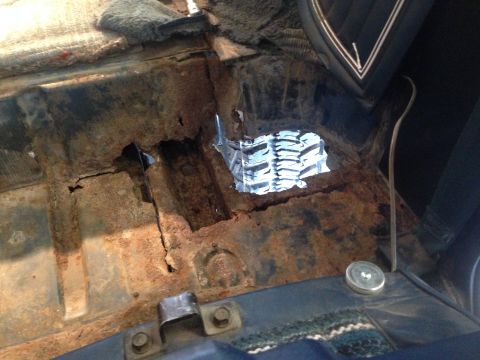 1979 Ford Bronco - The interior floor of a vehicle shows extensive rust and damage, with a large hole exposing the underside. A piece of reflective material i…