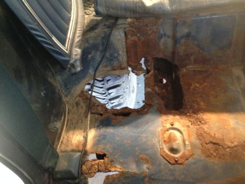 1979 Ford Bronco - This image shows the heavily rusted interior floor pan of a vehicle, with significant holes and corrosion visible. A portion of a dark blue…