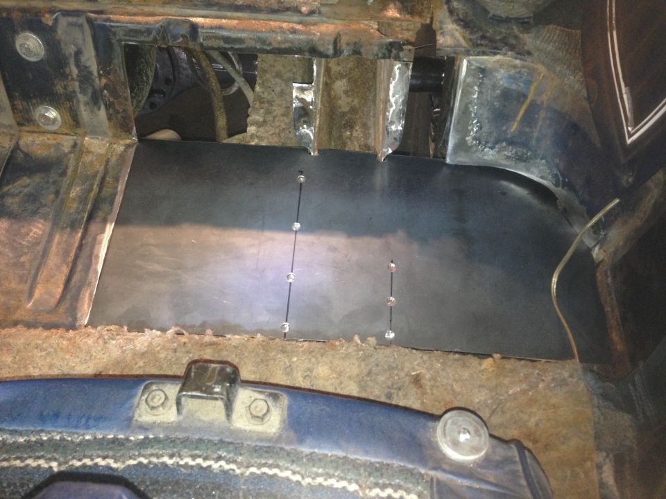 Custom metal floor panel installed in a vehicle interior with visible rivets and rust.