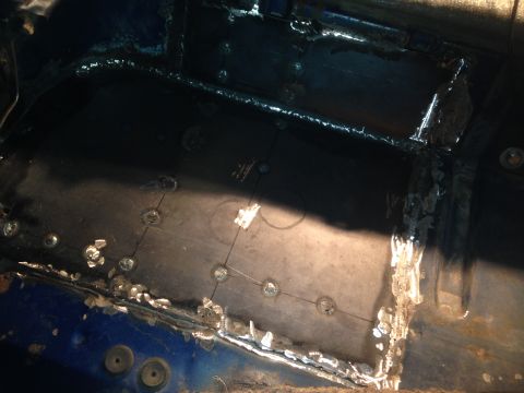 1979 Ford Bronco - The interior floor of a vehicle shows extensive metalwork, including new patch panels and numerous welds. Several circular indentations, li…