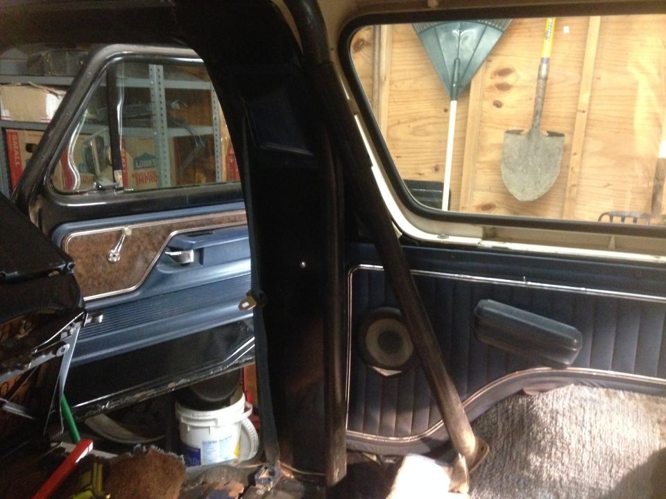 Interior of a vintage Ford Bronco showing door panel, roll bar, and tools outside window.