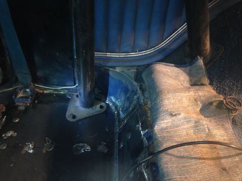 1979 Ford Bronco - The interior of a vehicle shows a blue upholstered seat and a black roll cage support post mounted to the floor. The floor appears to be da…