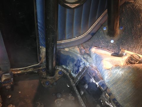 1979 Ford Bronco - Interior view of a vehicle's floor area, showing a roll cage support post bolted to the floor with blue fasteners. The area appears to be u…