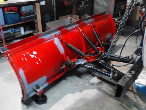 1973 Ford F-250 - A red snow plow is mounted to a black metal frame. The plow has visible springs and a chain attached.