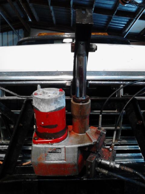 1973 Ford F-250 - A close-up view of a hydraulic pump assembly, likely for a snow plow, mounted on the front of a white Ford F-250. The pump has red and silv…