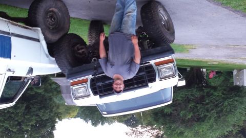Man standing upside down in front of a lifted white pickup truck with large tires.