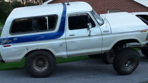 Lifted white 1979 Ford Bronco with blue stripe, side view, large off-road tires.