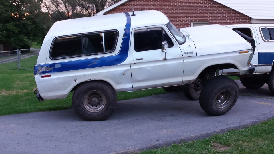 Lifted white 1979 Ford Bronco with blue stripe on a driveway.