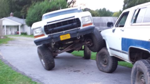 Lifted white Ford Bronco parked on driveway, front end angled up.