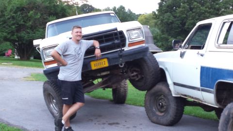 Man leaning on a lifted white Ford pickup truck.
