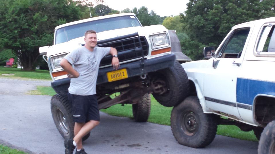 Man leaning on a lifted white Ford pickup truck.