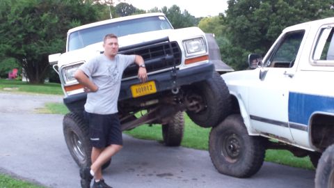 Man leaning on a lifted white Ford Bronco with large tires, another vehicle beside it.