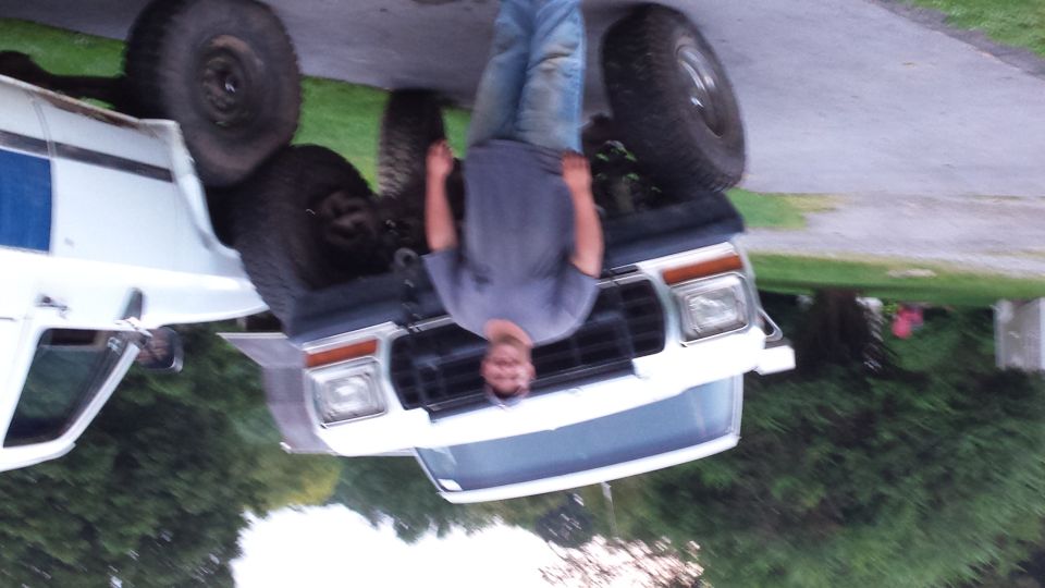 Man standing next to a white pickup truck tilted on its side.