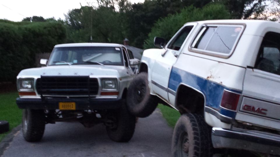 Lifted 1979 Ford Bronco next to a lifted white GMC SUV