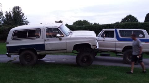 Two lifted SUVs parked side-by-side, with a man walking past the one on the right.