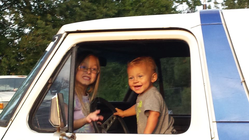Two children in the driver's seat of a white vehicle with blue trim.
