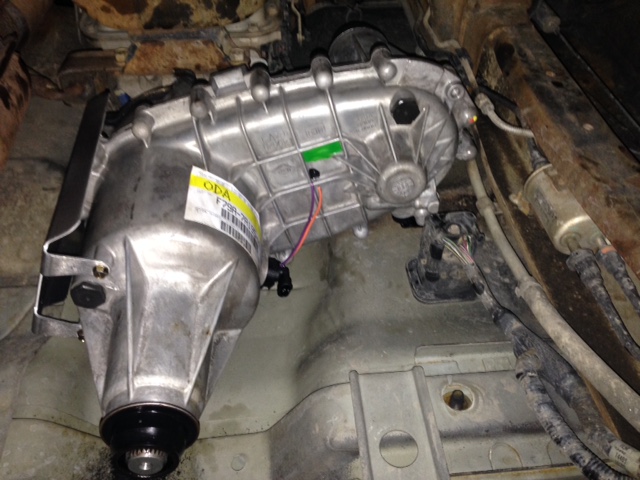 Underside view of a silver aluminum transfer case assembly on a vehicle.