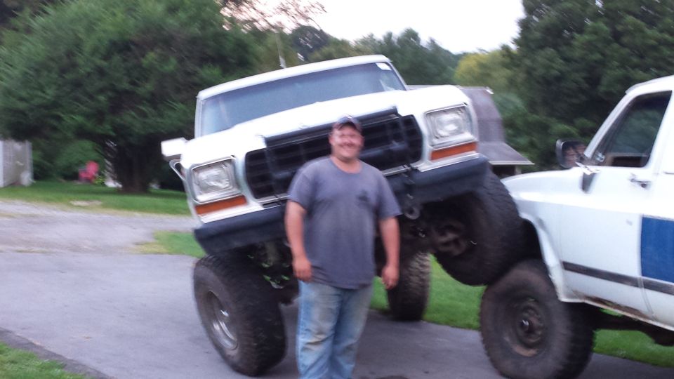 Man standing in front of a lifted white Ford truck on top of another truck