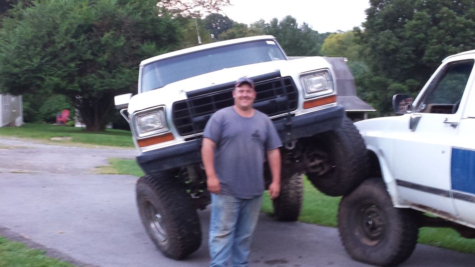 Man standing in front of a lifted white Ford Bronco with large tires, another truck to the right.