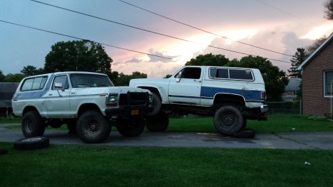 Two lifted SUVs, a Ford Bronco and a Chevrolet K5 Blazer, parked on a driveway.
