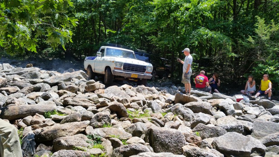 White 1970s Ford pickup truck driving over rocks with people watching.