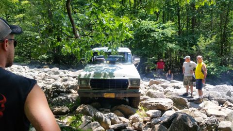 1979 Ford Bronco - A light green 1979 Ford Bronco is navigating a rocky terrain with several people standing around it. The vehicle is positioned front-on, su…