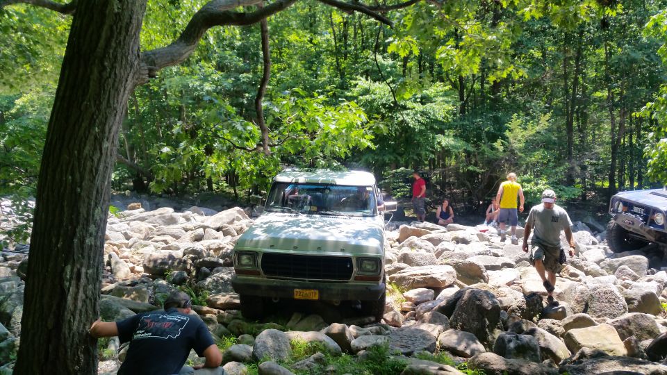 1979 Ford Bronco driving over rocks in a forest.