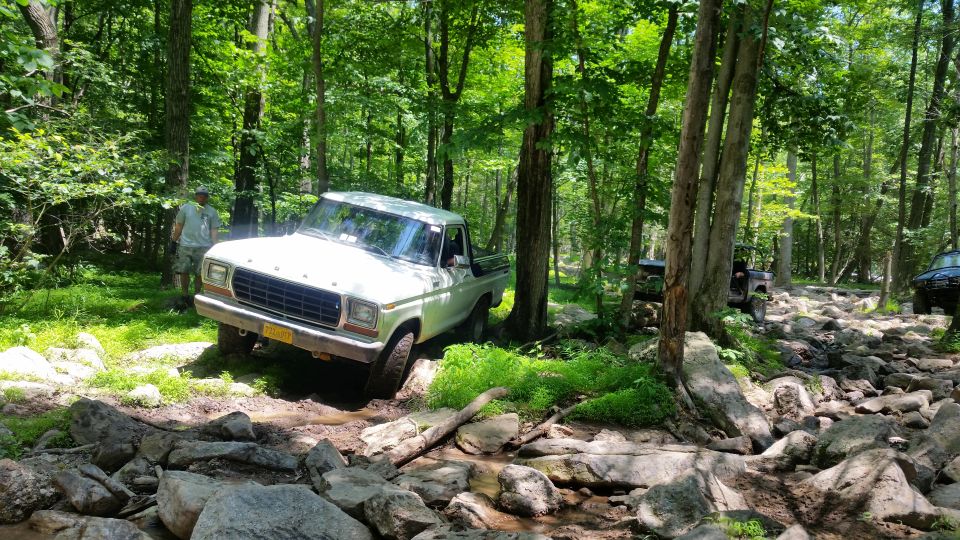 White Ford pickup truck driving on a rocky trail in a forest.