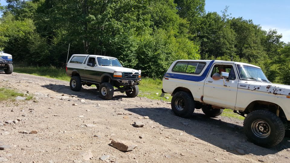 Two lifted Ford Broncos on a gravel road.