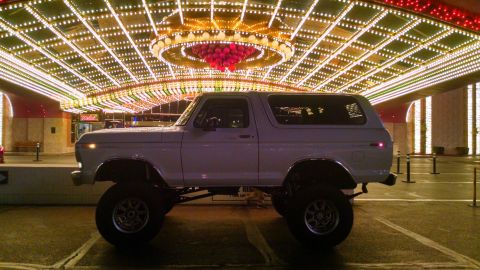1979 Ford Bronco - A lifted, white, two-door Ford Bronco is parked at night under a brightly lit, ornate canopy adorned with numerous lights. The vehicle is p…