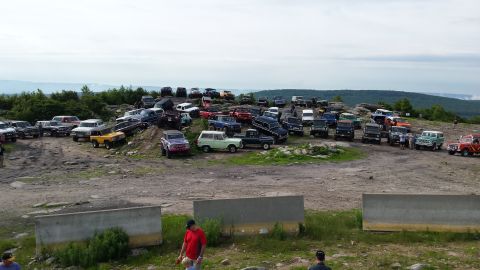 1979 Ford Bronco - A large collection of classic Ford Broncos and other off-road vehicles are parked on a rocky, elevated terrain with a scenic view of rollin…