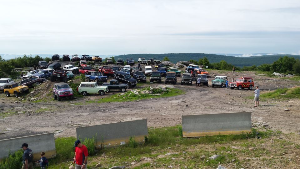 A large group of vintage off-road vehicles, including Ford Broncos and trucks, parked on a rocky hilltop.
