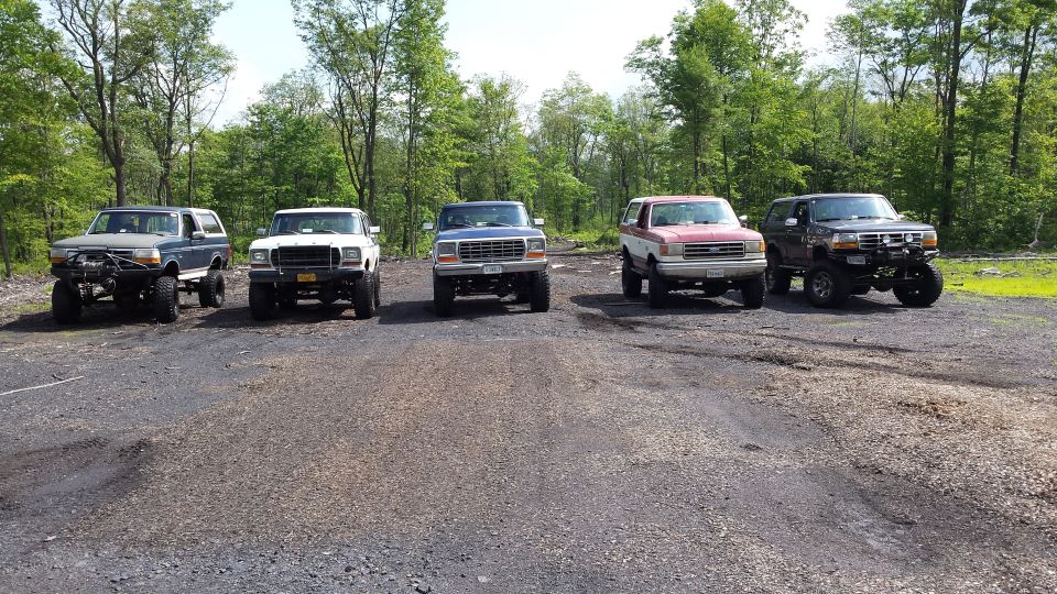 Five lifted Ford Broncos and trucks parked in a gravel lot.