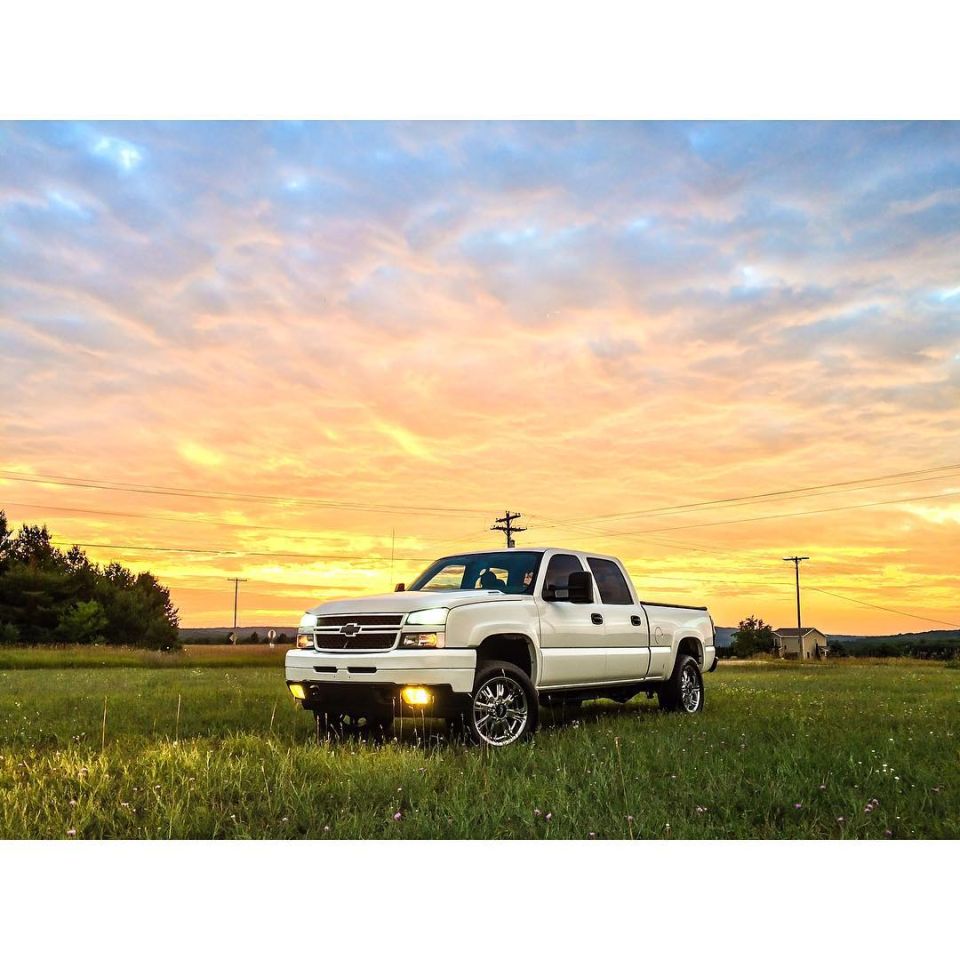 White Chevrolet Silverado 2500 pickup truck in a field at sunset.