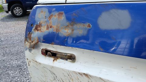 1979 Ford Bronco - A close-up view of the rusted rear corner of a blue and white pickup truck bed. The area shows significant rust damage and primer patches,…