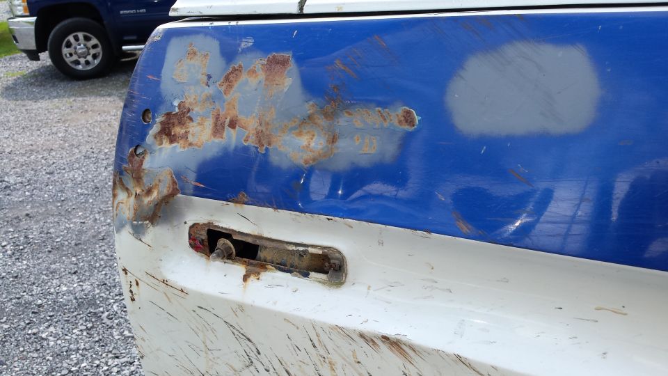 Close-up of rusted blue and white pickup truck bed corner with mounting bracket.