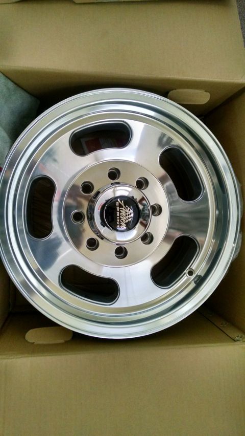 1979 Ford Bronco - A polished aluminum wheel with a black and chrome center cap is shown inside a cardboard box. The center cap has text that reads "American…